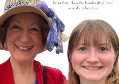 Grandmother wearing a custom floppy hat with a handcrafted band, smiling beside her granddaughter while choosing headwear together at an outdoor festival.