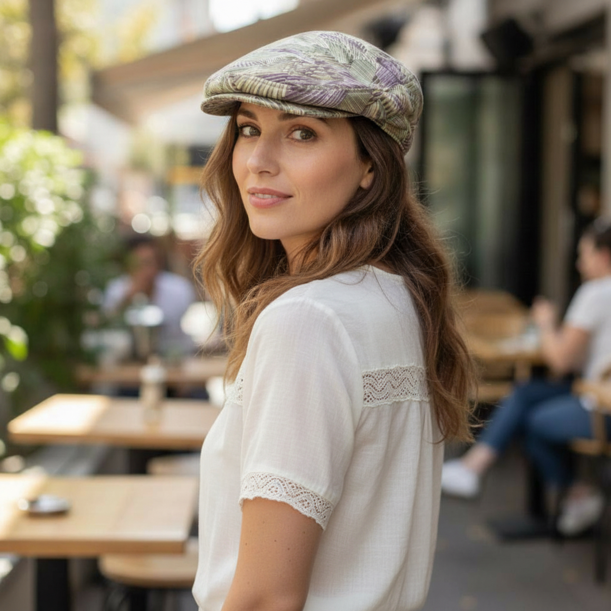 Woman wearing an Ivy Flat Cap in a green, purple, cream, and gold swirl print while seated outdoors at a café